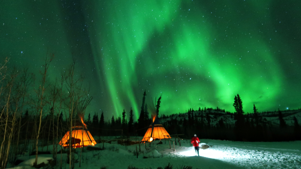 Aurora Borealis with starry sky above heated viewing lodge in Yellowknife, capturing clear 2026 winter conditions.