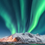 Vibrant green Northern Lights dancing over Tromsø fjords and mountains in Norway during solar maximum 2026